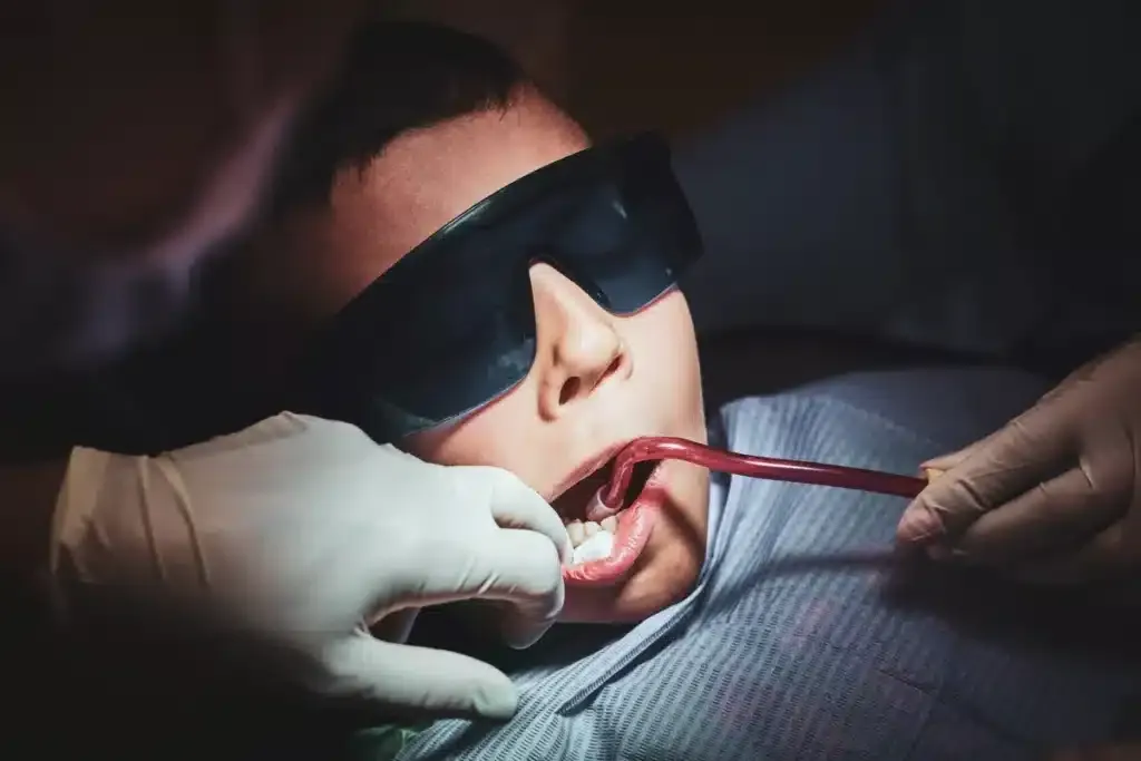Child wearing protective glasses at a dental checkup with a dentist holding tools.