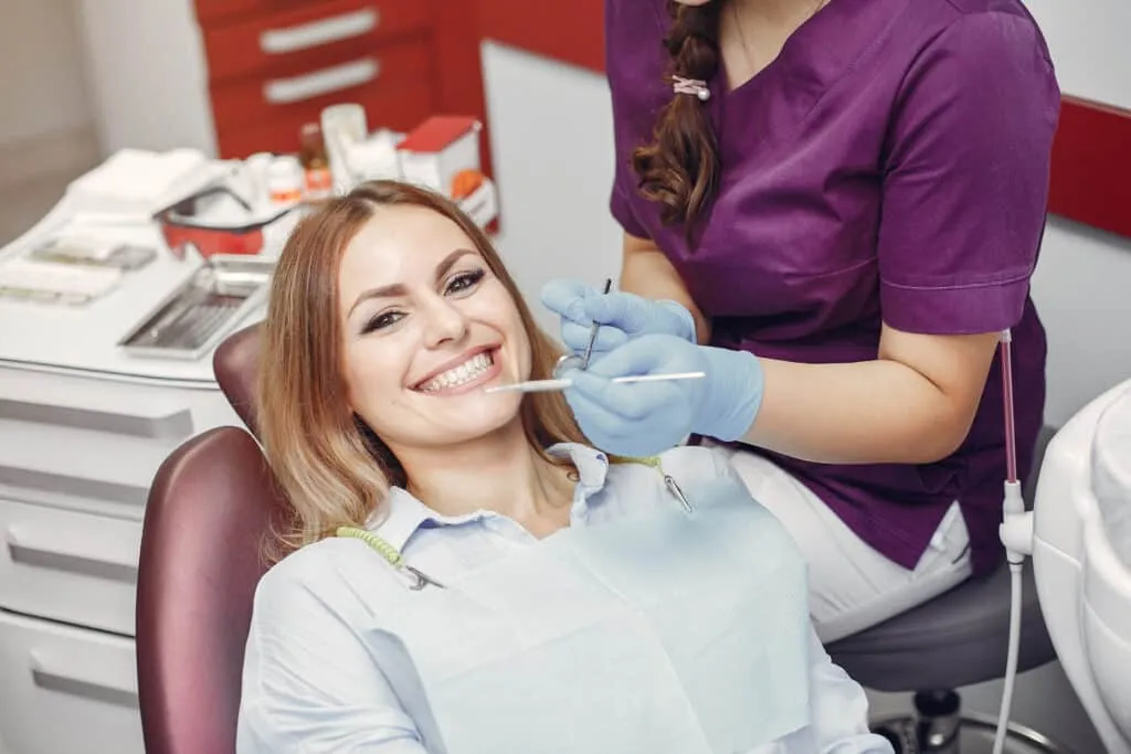 Smiling patient in a dental chair with a dentist holding tools during a checkup