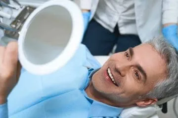 Man smiling, holding mirror, after dental procedure.